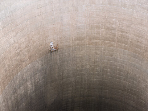 Aerial view of the interior of a large concrete cooling tower with a small maintenance platform suspended against the curved wall in the United Kingdom.
