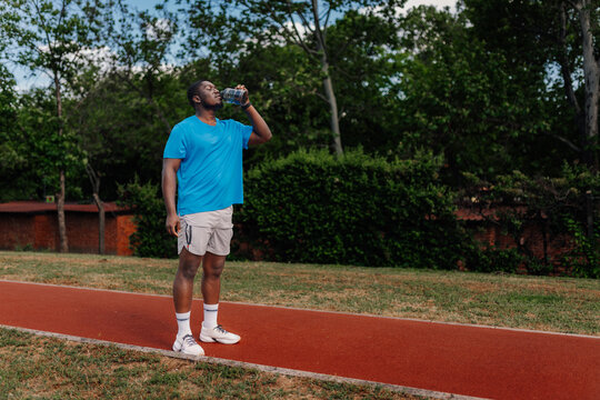 Black man drinking water after fitness training outdoors