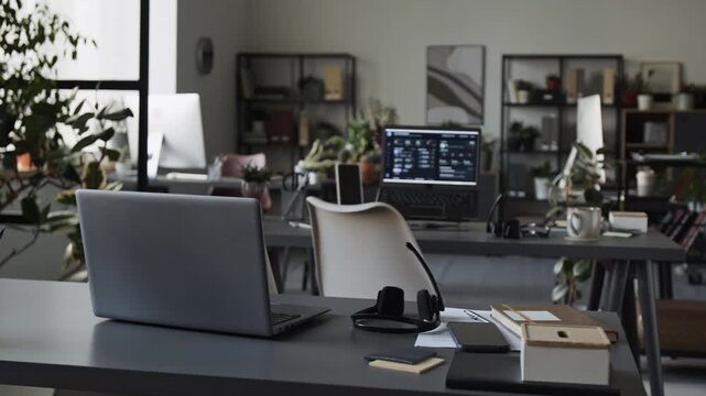 Empty office workstations displaying laptops, headsets, and notebooks on desks. Footage serves well for corporate communications, remote work, or business technology marketing