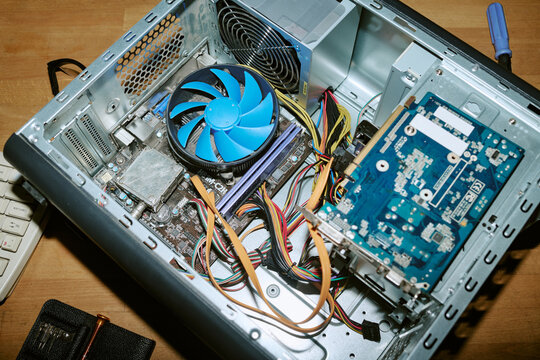 High angle shot of open vintage computer chassis showing motherboard, blue cooling fan, and messy wiring. Image represents hardware repair, retro computing, and Information Technology support services