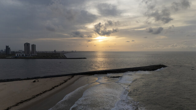 Aerial view of Tarkwa Bay Beach at sunset with gentle waves hitting the breakwater and the Lagos skyline visible in the distance in Lagos, Lagos, Nigeria.