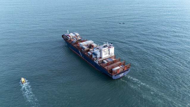 Aerial view of a large container ship navigating the open sea near the coast with a small pilot boat trailing behind in Lagos, Lagos, Nigeria.