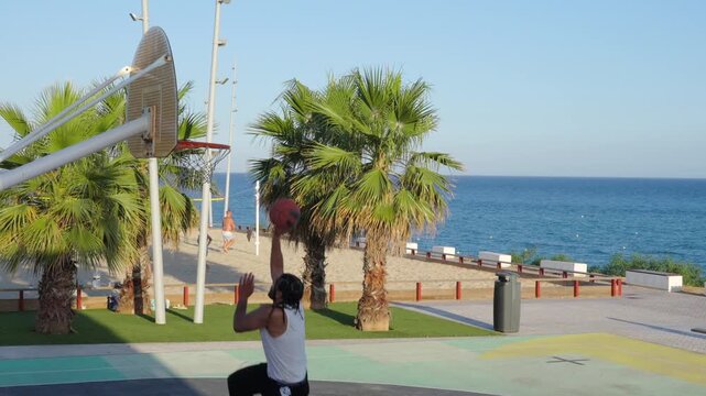 Young man shooting baskets at outdoor seaside court