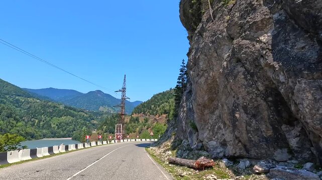 Cliffside highway provides access, wide view beside Jvari Reservoir with exposed rock walls and roadside debris in Georgia, documenting geotechnical risk, route maintenance and transport safety