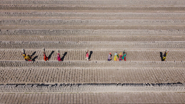 Aerial view of workers carrying bricks through rows of drying clay bricks at a brick field in Dhaka, Bangladesh.