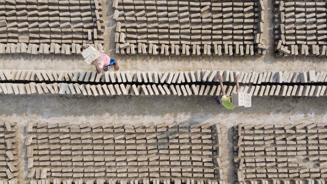Aerial view of brick field with workers carrying bricks in rows in Dhaka, Bangladesh.