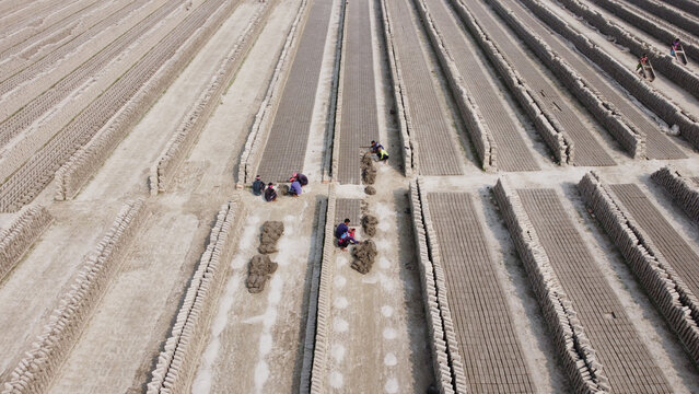 Aerial view of workers arranging rows of clay bricks in a large brick field in Dhaka, Bangladesh.