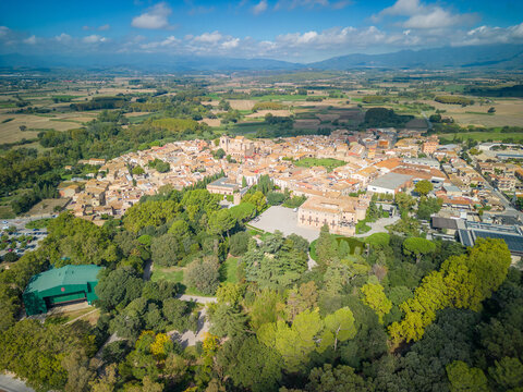 Aerial view of the historic Castell de Peralada surrounded by lush gardens, stone buildings, and terracotta rooftops in the town of Peralada, Catalonia, Spain.