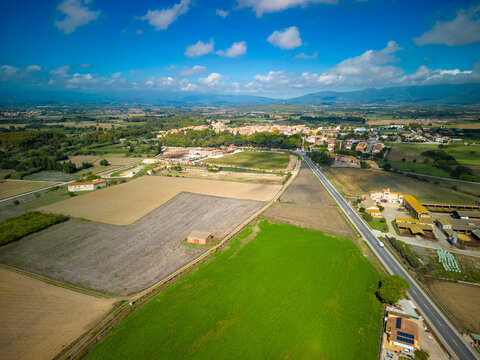 Aerial view of the historic town of Peralada surrounded by agricultural fields, vineyards, and rural landscapes under a blue sky in Peralada, Catalonia, Spain.