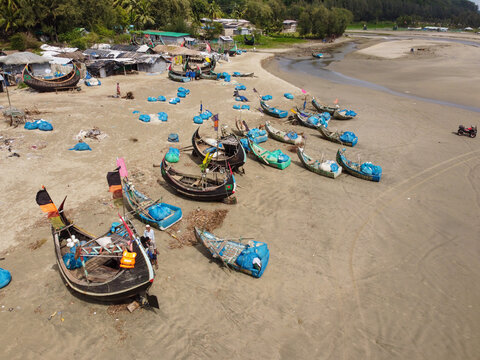 Aerial view of traditional wooden fishing boats resting on the sandy beach at low tide with colorful flags and small huts in the background in Cox's Bazar, Chittagong Division, Bangladesh.