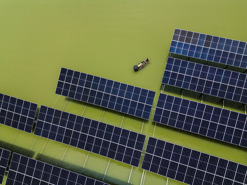 Aerial view of Sirajganj 68MW Solar Park with floating solar panels on green water and a small boat navigating between the arrays in Sirajganj, Rajshahi Division, Bangladesh.
