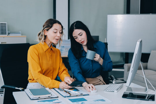 Two businesswomen discussing work using a laptop in a modern office lounge area, showing teamwork and communication
