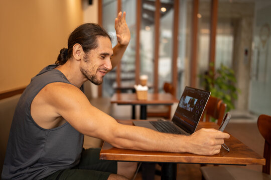 Man waving during video call at cafe working remote