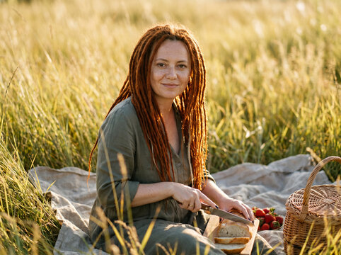 Woman picnic in a field slicing bread from a basket on a blanket for natural lifestyle wellness background and countryside banner
