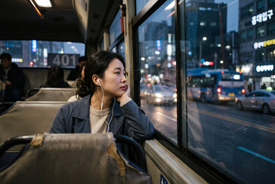 Woman sitting on city bus looking out window at night traffic for urban commute background and contemplative lifestyle scene