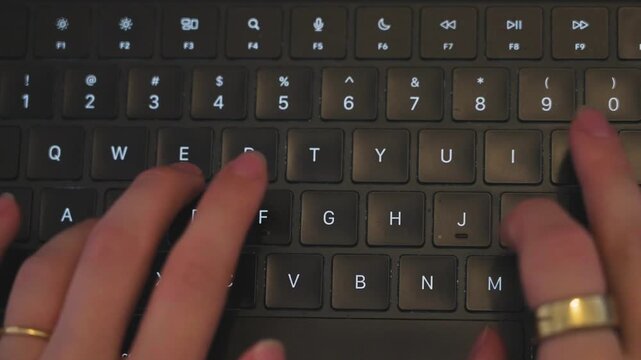 Hands typing quickly on backlit computer keyboard close up shot.