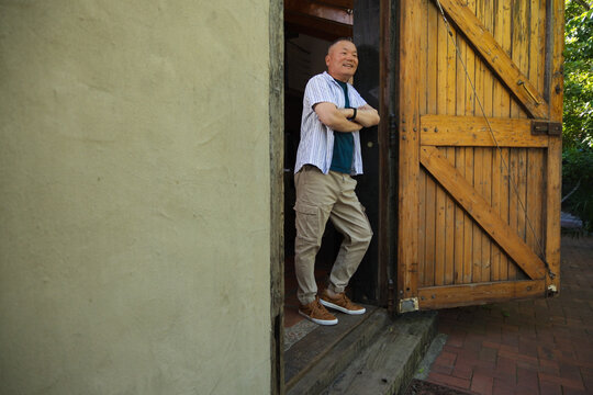 Senior Asian man leaning in doorway by stucco wall, wearing striped shirt and watch, copy space