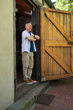 Senior Asian man standing in doorway, crossing arms, wearing striped shirt, barn gate, copy space
