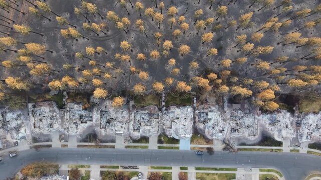 Spokane wildfire damage in Washington showing a top-down descending aerial view of a row of burned homes with charred trees behind them after the 2026 fire.