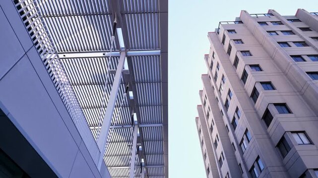 Low-angle walking view revealing modern university architecture at the UC Berkeley campus in California, showcasing geometric building facades and a concrete high-rise against a clear sky