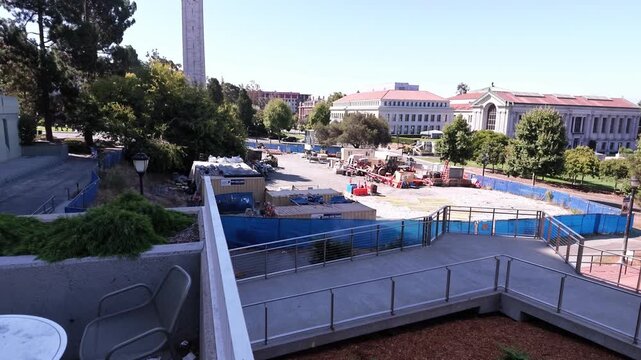 Panoramic view from a terrace revealing the Sather Tower and the historic campus of the University of California, Berkeley, with a construction site in the foreground on a sunny day