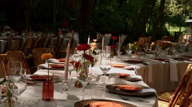 Long linen tables dressed with rattan chargers bud vases and tapers in a shaded garden