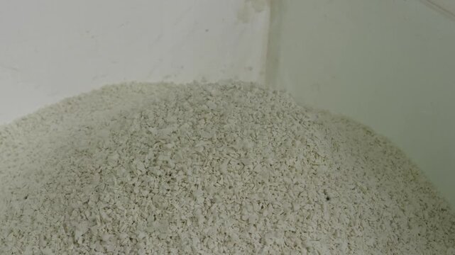 Ground plastic granules piling into a mound inside a white container at a Recycling Factory