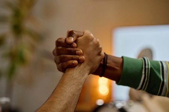 Close up of multiethnic male football fans clasping hands in celebration, representing unity and friendship. Image is suitable for sports marketing and social diversity campaigns