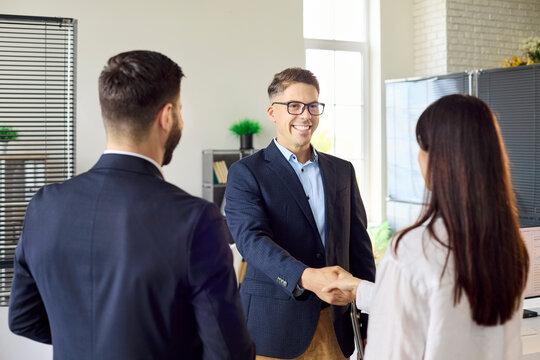 Businesspeople handshake in office partnership meeting. Confident manager greets a colleague as colleagues watch, showing trust, teamwork and agreement. Concept of partnership, deal and success.