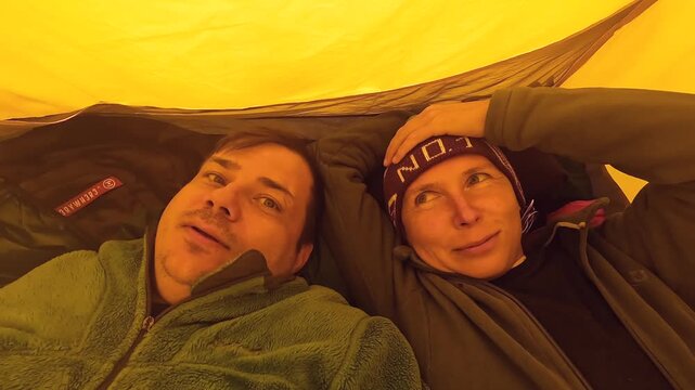 Two hikers rest, overhead close-up view, inside a tent after a demanding mountain trek in Svaneti, Georgia, supporting camping recovery, expedition shelter, outdoor partnership, travel wellness themes