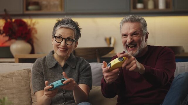 Funny middle-aged couple play video game with gamepads as a team at home