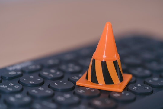 Cybersecurity warning concept with orange traffic cone on computer keyboard symbolizing online danger, system maintenance, digital risk, network security, data protection and technical issues.