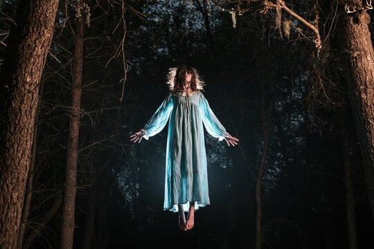 Eerie girl levitates in dark forest at night, embodying Halloween spirit