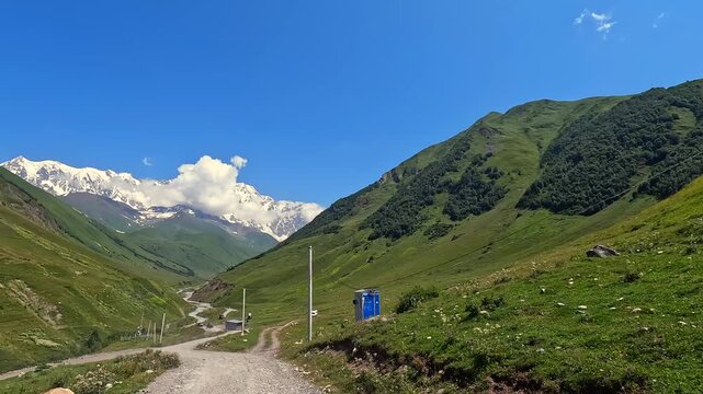 Car approaching Mount Shkhara in wide view along a gravel road from Ushguli, Georgia, presenting trailhead access for glacier trekking, guided excursions and highland destination marketing