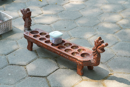 Traditional Indonesian carved wooden Congklak (Mancala) game board on outdoor paving blocks.