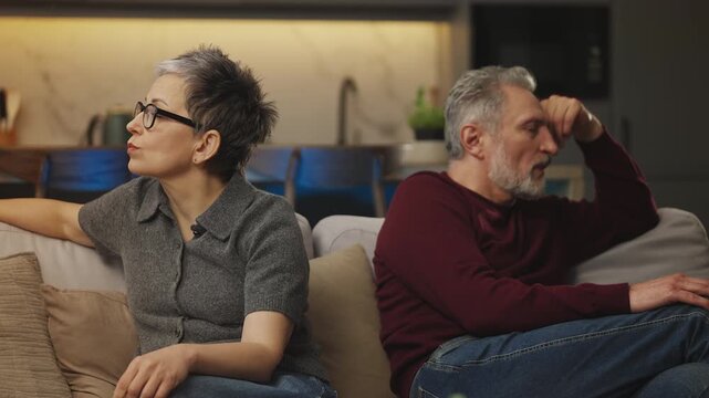 Depressed mature couple sit apart on sofa after conflict, relationship issues