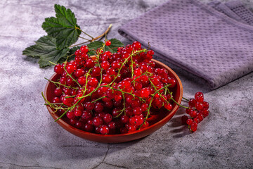 Fresh red currants in wooden bowl on stone surface with green leaves and purple cloth © Andrei Starostin