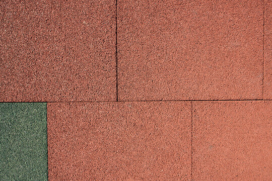 Outdoor daytime shot of an elastic terracotta safety playground tile surface exhibiting coarse granulation