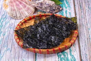 Nori seaweed sheets on woven bamboo tray with seashells on weathered wood © Andrei Starostin