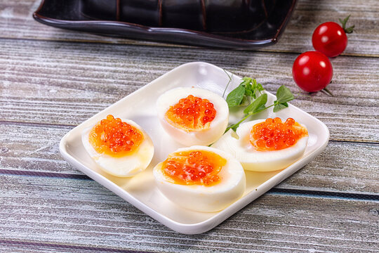 Deviled eggs topped with red caviar on white plate with cherry tomatoes and microgreens