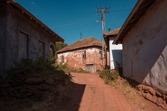 Dirt road leading through Topli Do village with stacked firewood and traditional mud houses at the foot of a sunny hill in Stara Planina nature reserve, Serbia.