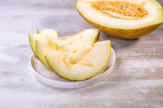 Sliced piel de sapo melon on white plate with half melon in background