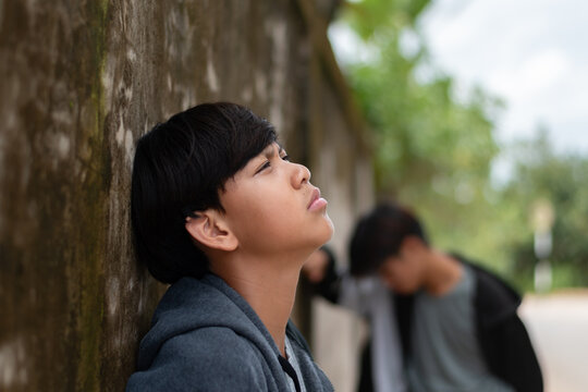 A stressed and sad teenage boy leaning against an old wall, looking up with a depressed expression, feeling exhausted from family pressure or bullying.