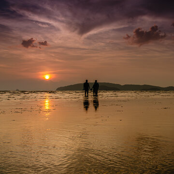 People gather on a tidal flat, gathering shellfish and enjoying the sunset.