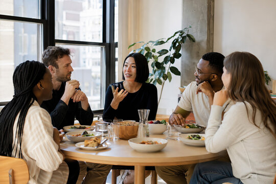 Five diverse individuals converse animatedly around a rustic, light-colored wooden table. Photograph depicting a group of individuals engaged in conversation around a table.