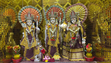 Obraz premium Gilded altar with three ornate statues of Hindu deities adorned with garlands and umbrellas.
