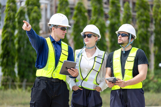 Oil refinery engineers team with tablet pointing at industrial plant, Petroleum plant workers in safety gear discussing work outdoor with tablet, Energy industry professionals inspecting facility site