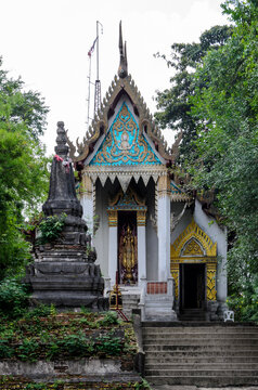An exterior photo of an ancient temple at Wat Khao Yi San, Thailand, with a pagoda and an old Buddha statue, in the attitude of stopping the rainstorm on a cloudy day