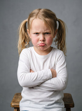 4-year-old Caucasian girl looking visibly angry and unhappy, pouting lips, furrowed eyebrows and arms crossed, children's emotions concept