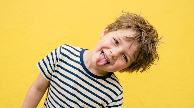 Boy sticking out tongue and smiling with messy hair on a bright yellow background